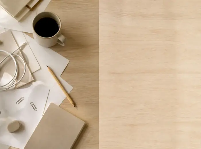 Bureau en bois clair vu de dessus, moitié gauche encombrée d’objets et de papiers, moitié droite entièrement vide