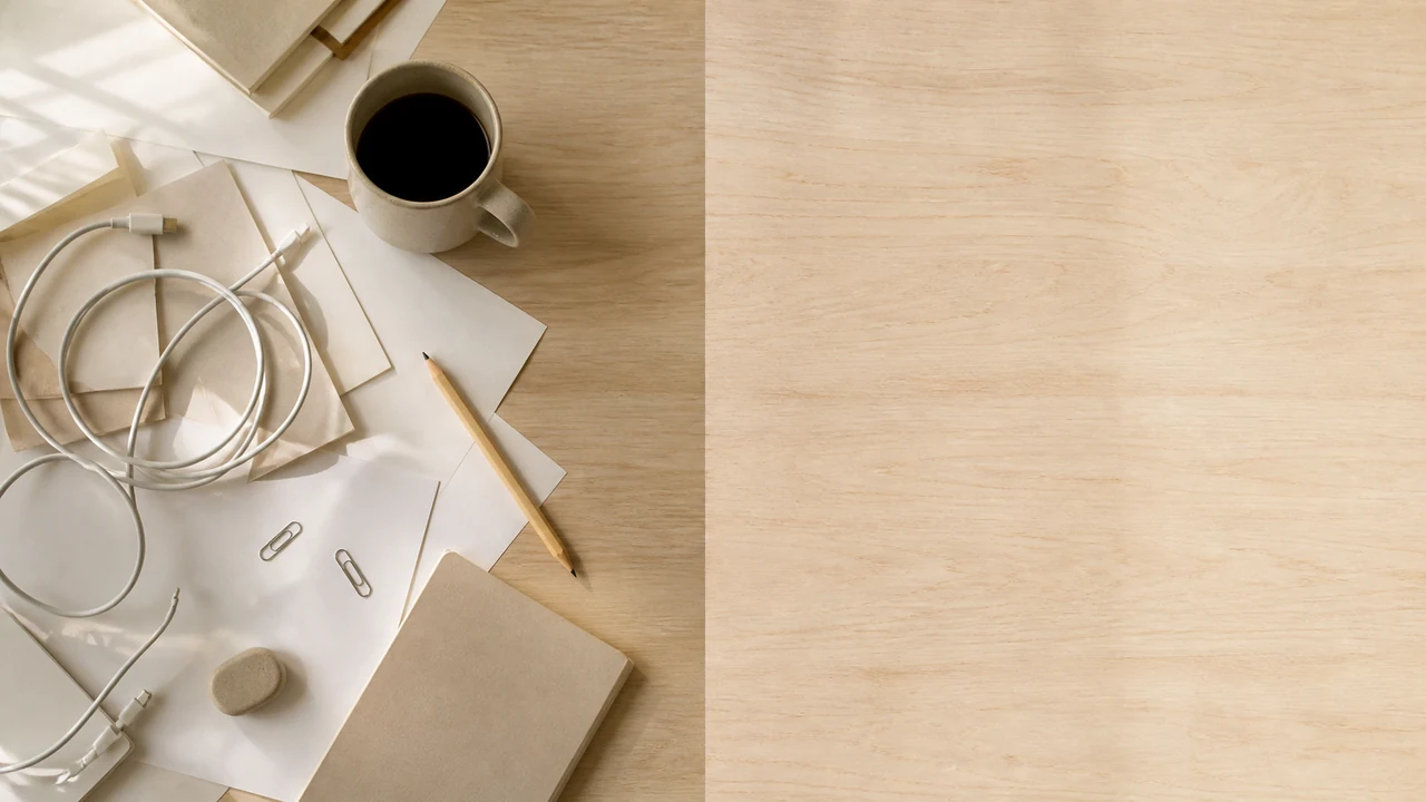 Bureau en bois clair vu de dessus, moitié gauche encombrée d’objets et de papiers, moitié droite entièrement vide