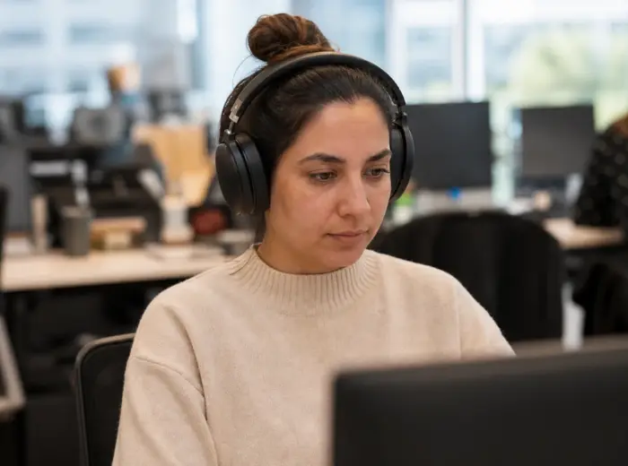 Personne au casque audio travaillant à un bureau dans un espace ouvert, collègues et postes fortement flous derrière