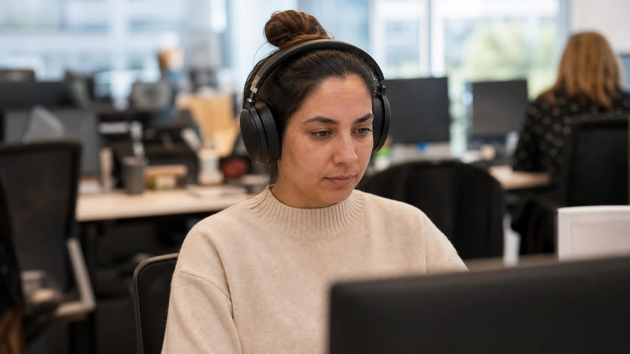 Personne au casque audio travaillant à un bureau dans un espace ouvert, collègues et postes fortement flous derrière