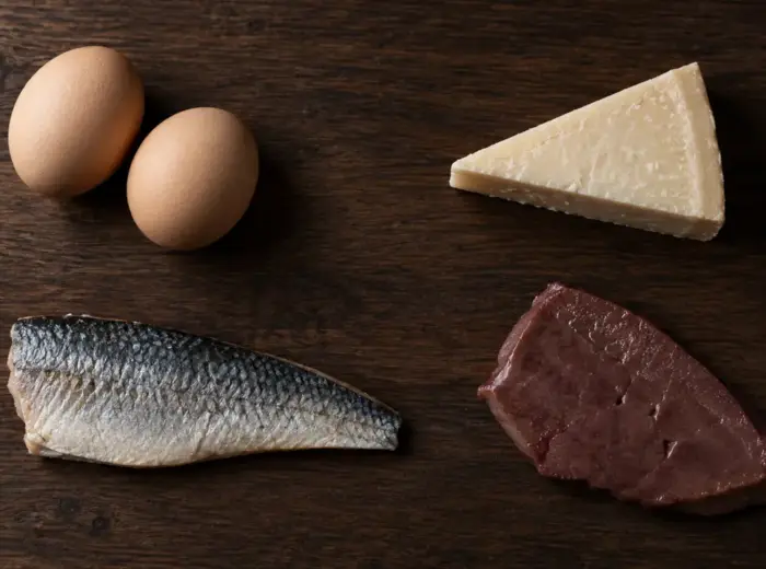 Deux œufs bruns, un morceau de fromage à pâte dure, un filet de poisson argenté et une tranche de foie, espacés sur une planche en bois foncé
